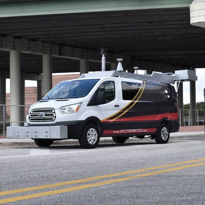 Van with equipment on front and top driving under an overpass