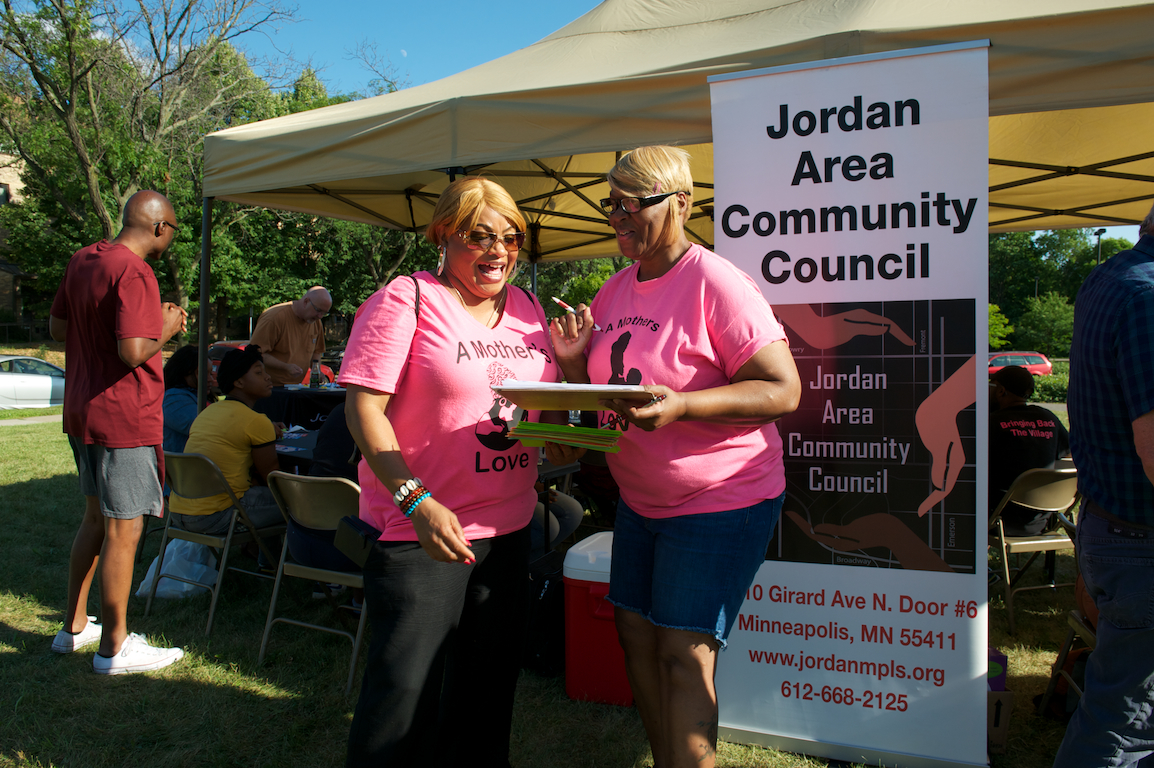Two women talking in front of Jordan Area Community Council table
