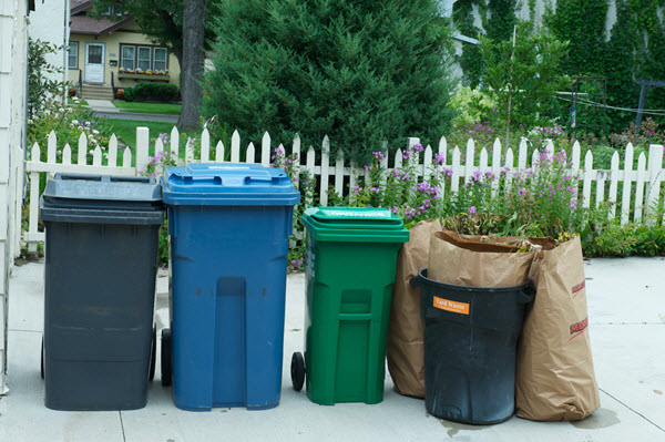 Garbage, recycling and organics carts and yard waste bags outside a home.