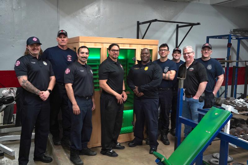 A group of firefighters pose in front of a donated sauna.