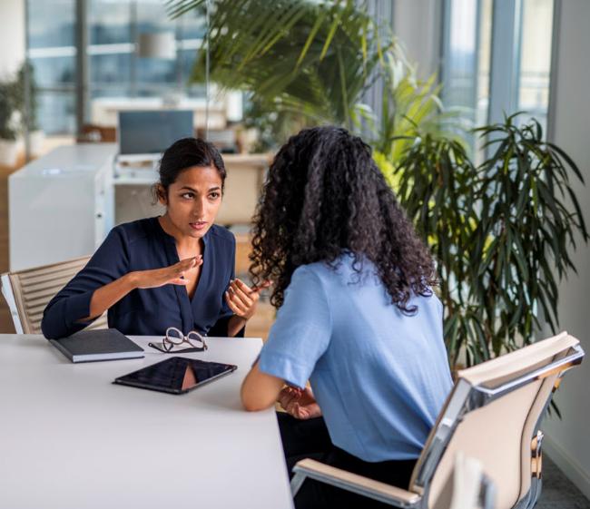 A person at an office table explaining something to another.