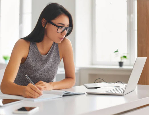 Woman with glasses looking at her laptop taking notes