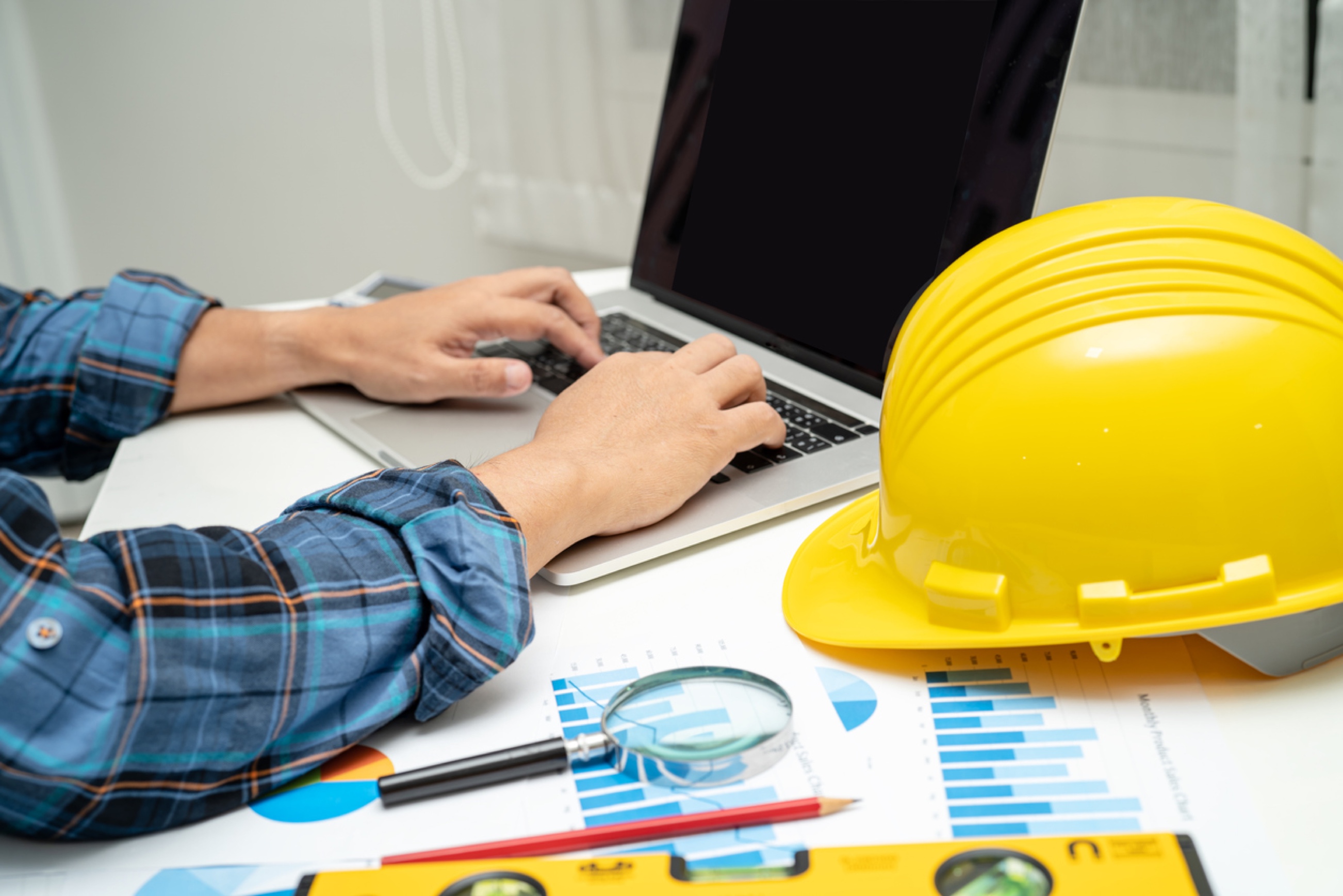 Hands on laptop near yellow construction hat