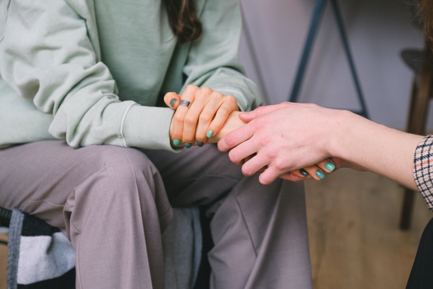 One person seated comforting and supporting another person seated across from them