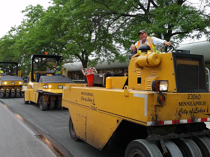 A work crew uses large machines to resurface a road.