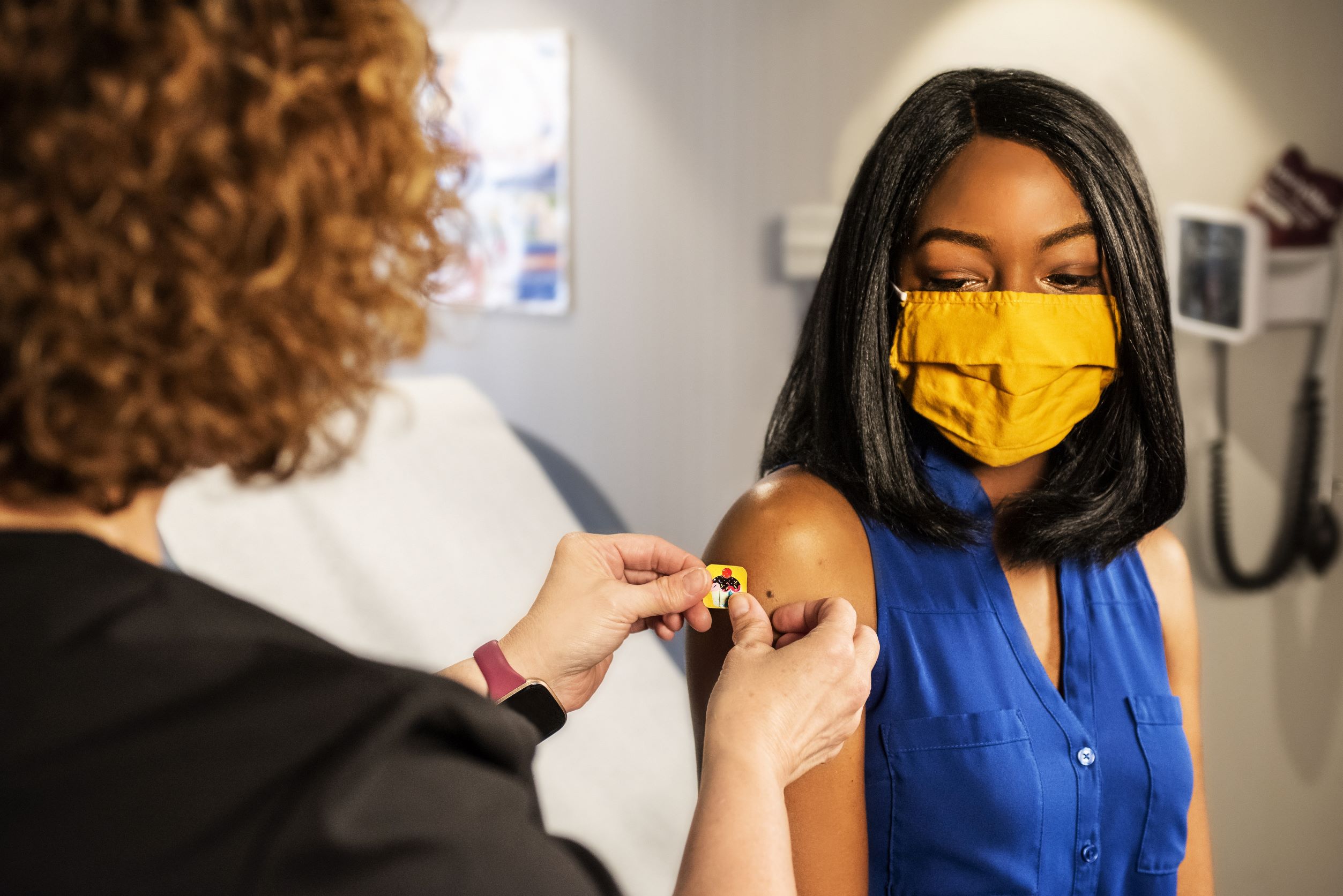 Young African American student with yellow mask receives a vaccine or shot in arm by a medical professional nurse Young African American student with yellow mask receives a vaccine or shot in arm by a medical professional nurse