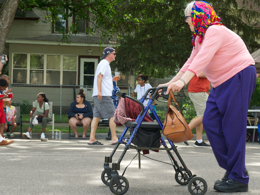Elderly woman walking down streets, people in background