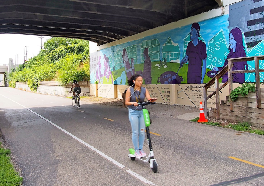 person riding scooter under tunnel with mural in background