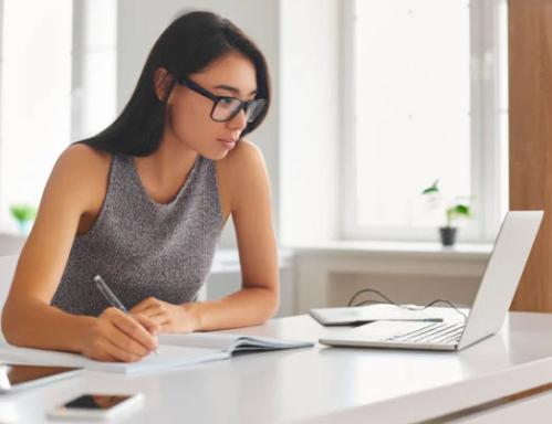Woman with glasses looking at her laptop taking notes