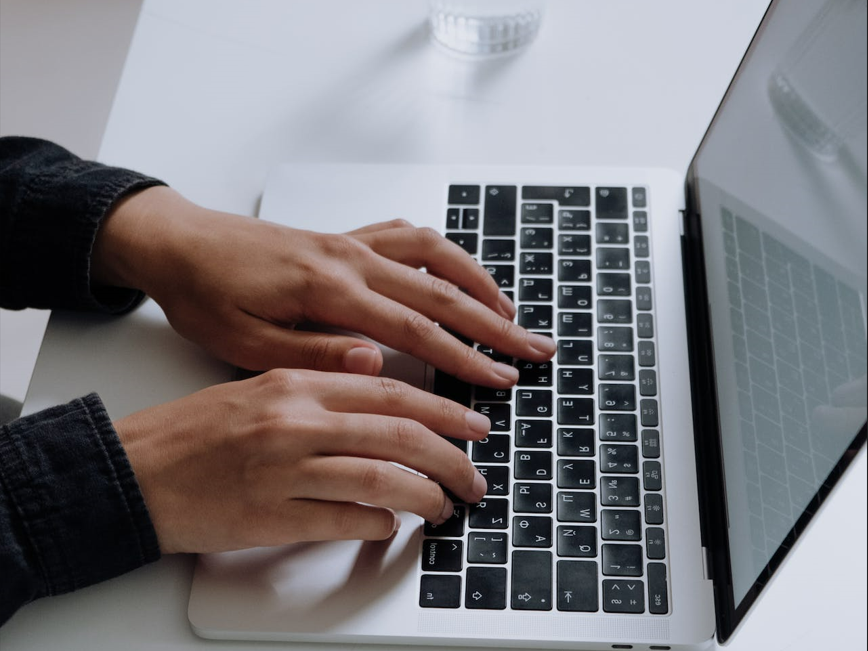 Hands typing on laptop beside glass of water Hands typing on laptop beside glass of water